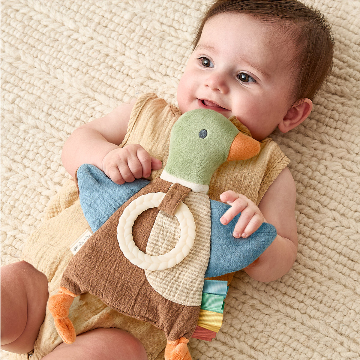  Lifestyle: smiling baby holding the Mallard Duck Crinkle Sensory Toy with silicone teething ring. 