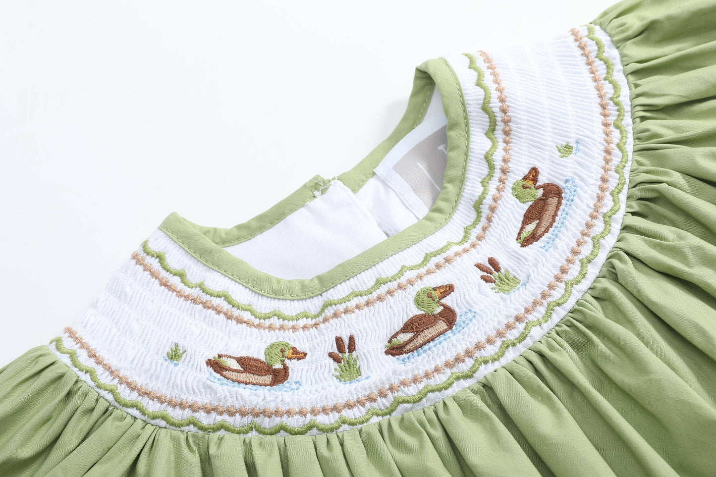 Close-up of a light green dress with a white smocked yoke featuring embroidered ducks and reeds.