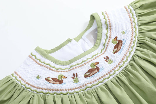 Close-up of a light green dress with a white smocked yoke featuring embroidered ducks and reeds.