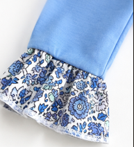 A close-up of a light blue garment with a ruffled hem featuring a blue and white floral pattern.
