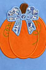 An orange pumpkin applique or embroidery design with a blue and white patterned bow on a light blue background.