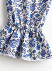 A close-up of a white fabric garment with a blue and green floral print, featuring a gathered waistband.