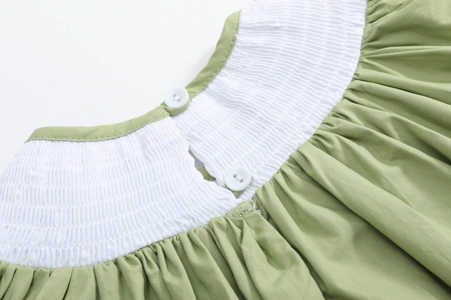 Close-up of a light green dress with a white smocked yoke and two white buttons, shown against a plain white background.