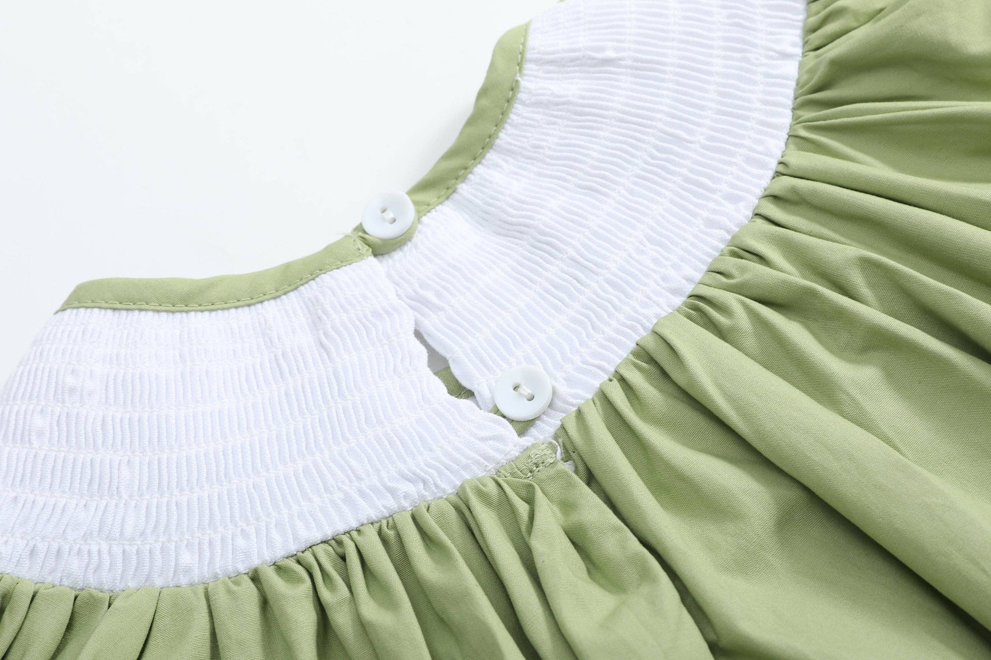 Close-up of a light green dress with a white smocked yoke and two white buttons, shown against a plain white background.