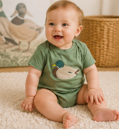 Baby boy wearing a sage green mallard duck appliqué bubble romper outdoors during a family gathering.